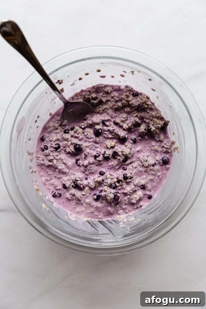 blueberry overnight oats before setting in the fridge in a clear mixing bowl with a spoon in it.