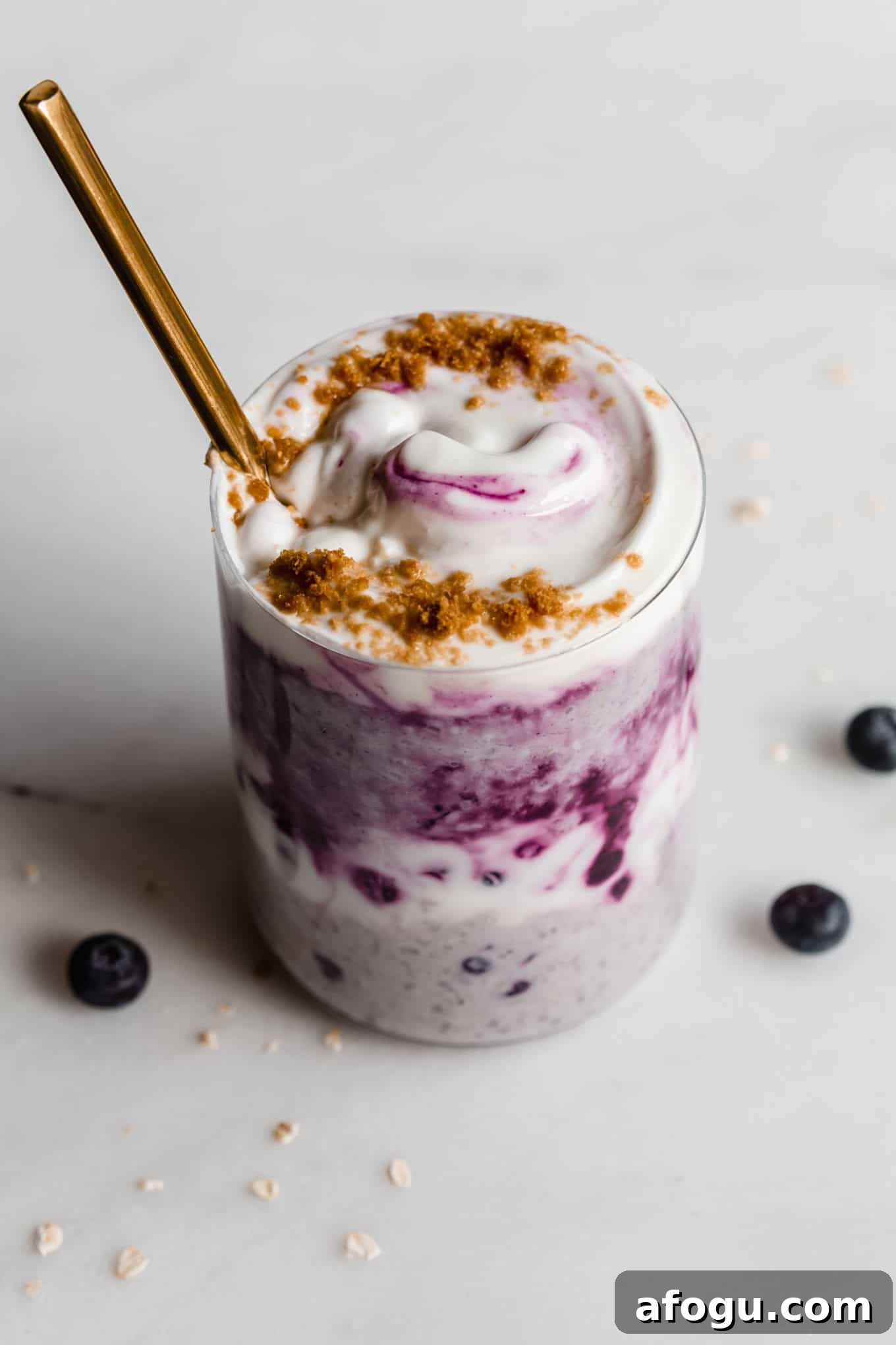Blueberry overnight oats in a cup topped with yogurt with a gold spoon in it.