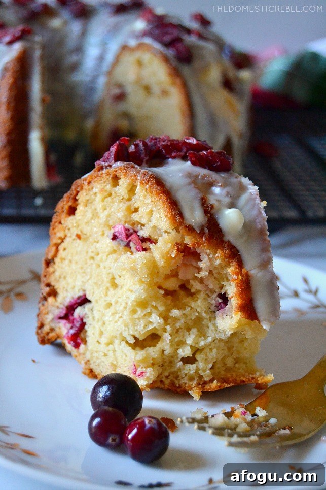 Piece of white choc cranberry bundt cake with a bite missing on a white plate with three cranberries
