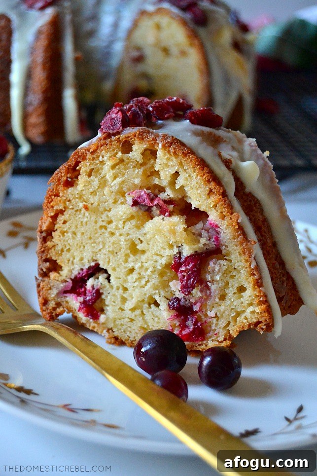 Slice of white choc cranberry cake on white plate with gold fork