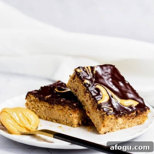 Two slices of peanut butter cake on a white plate. There is a spoon with peanut butter next to the cake.