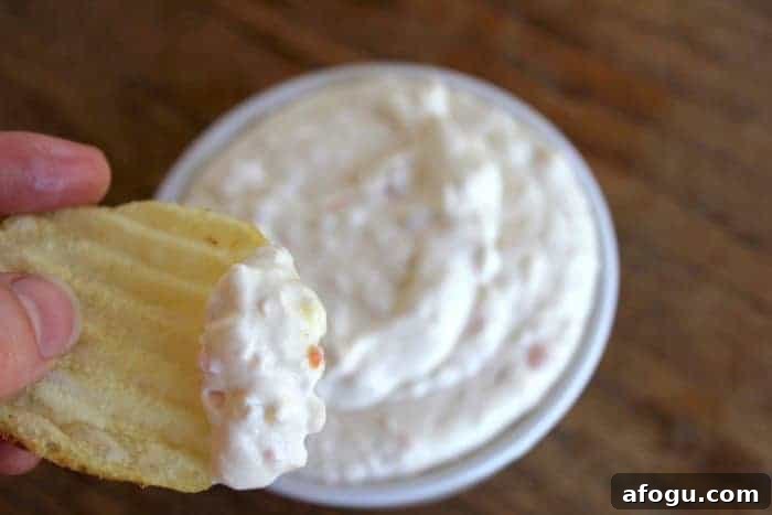 Image shows a hand holding a chip with dip over a bowl of dip