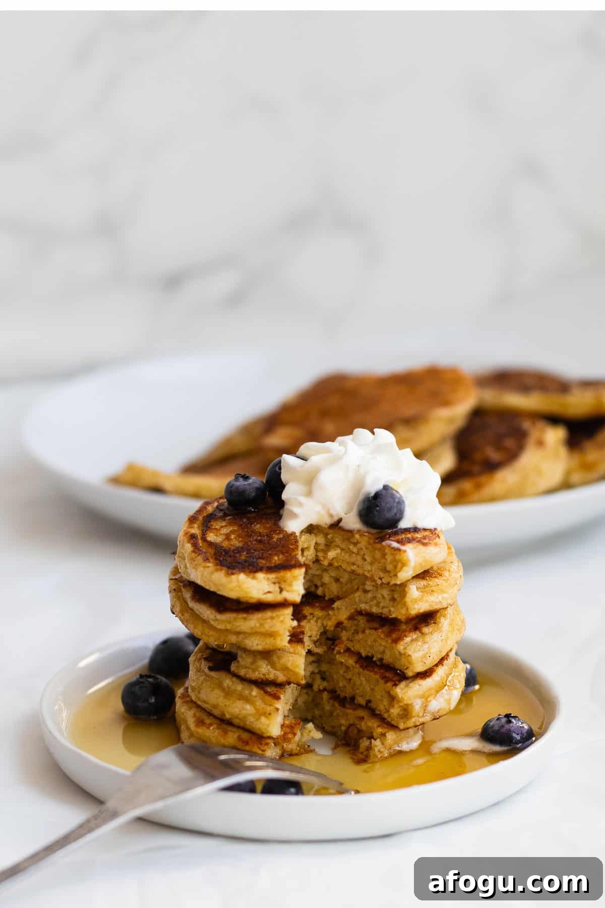 6-Ingredient Cottage Cheese Oatmeal Pancakes Recipe 2 stack of pancakes on a white plate with blueberries, syrup and whipped cream