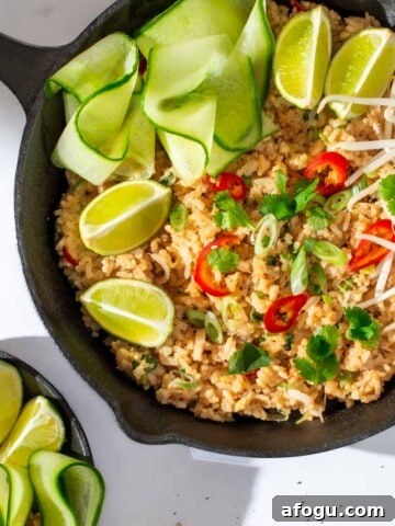 Khao pad in a black frying pan with cucumber ribbons and lime wedges.