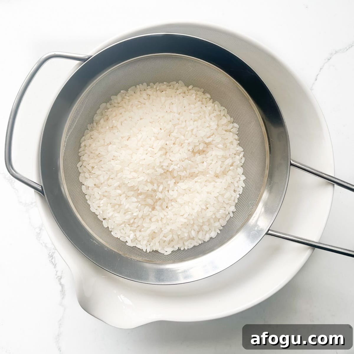 Sushi rice being washed through a sieve over a white bowl.