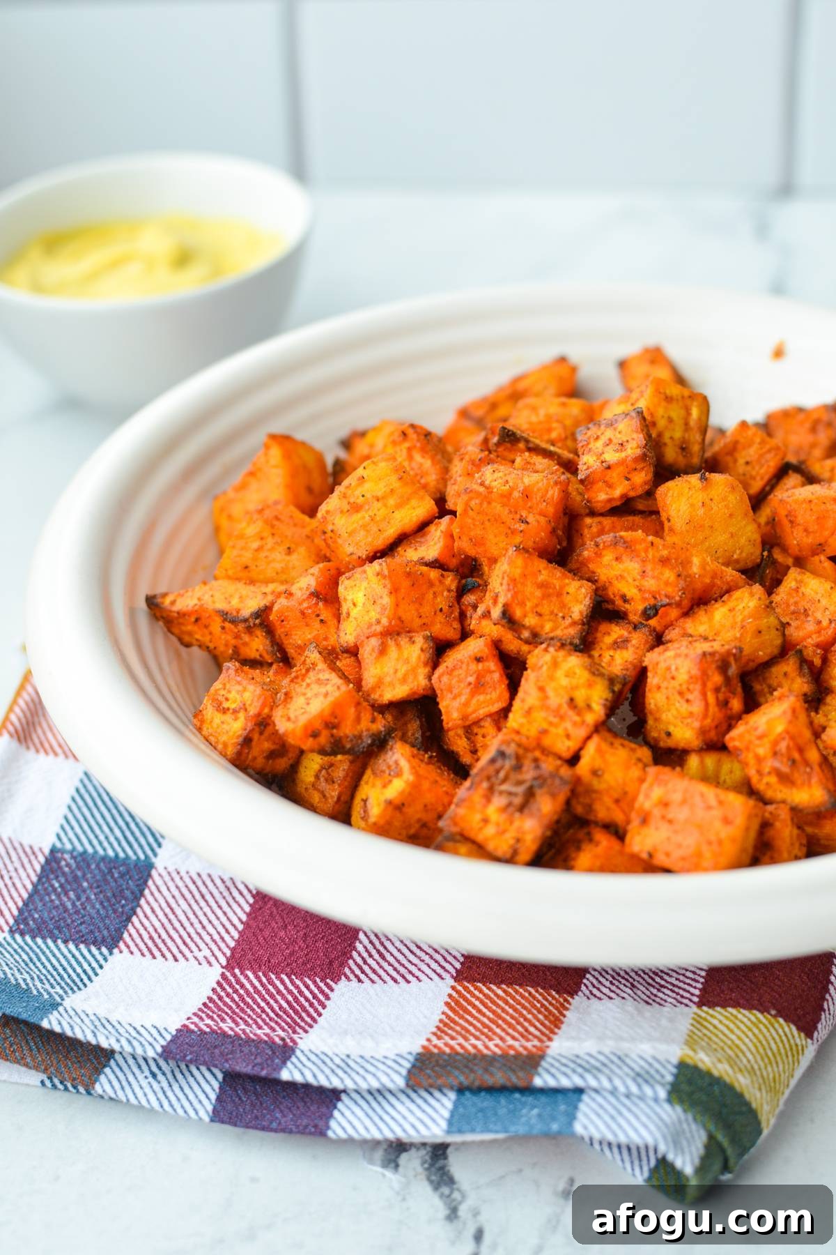 Crispy Air Fryer Sweet Potato Cubes Recipe 8 A bowl of roasted sweet potato cubes with a dipping sauce in the background.