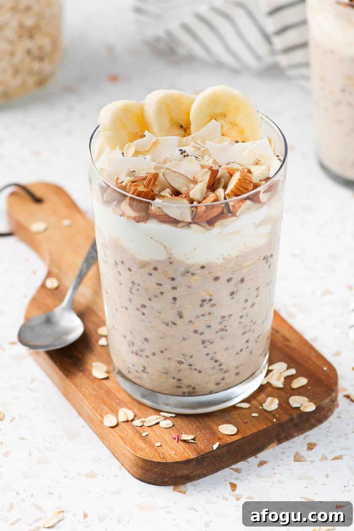 Glass jar of overnight oats, sitting on a wooden board, with a spoon on the edge.
