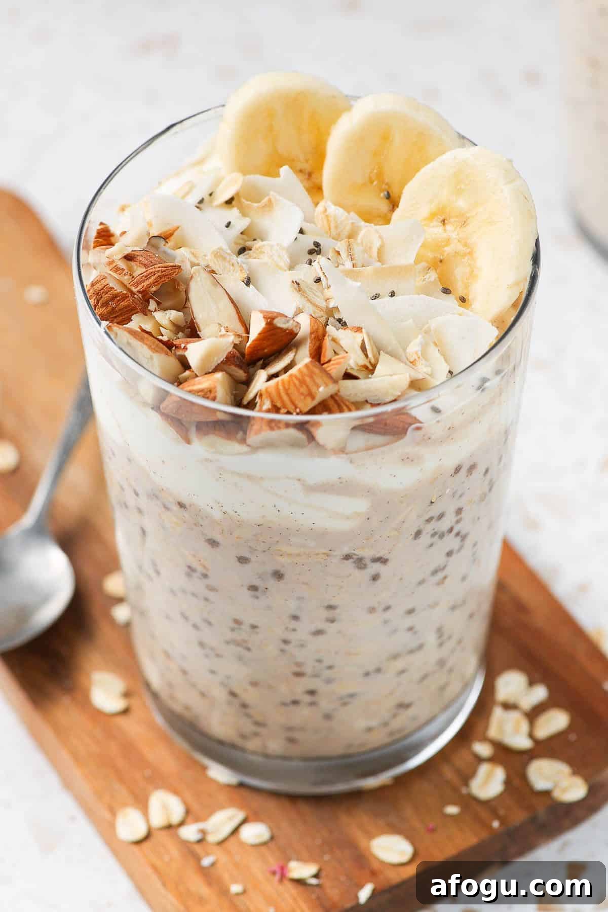 Glass jar of overnight oats, sitting on a wooden board, with a spoon on the edge.