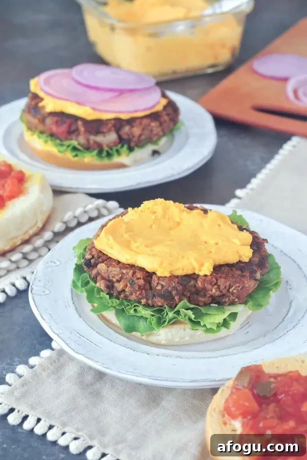 Salsa burgers sit on plates on a picnic table. Burger is dressed with curly lettuce, cheese sauce, salsa, purple onion slices and sesame seed buns.