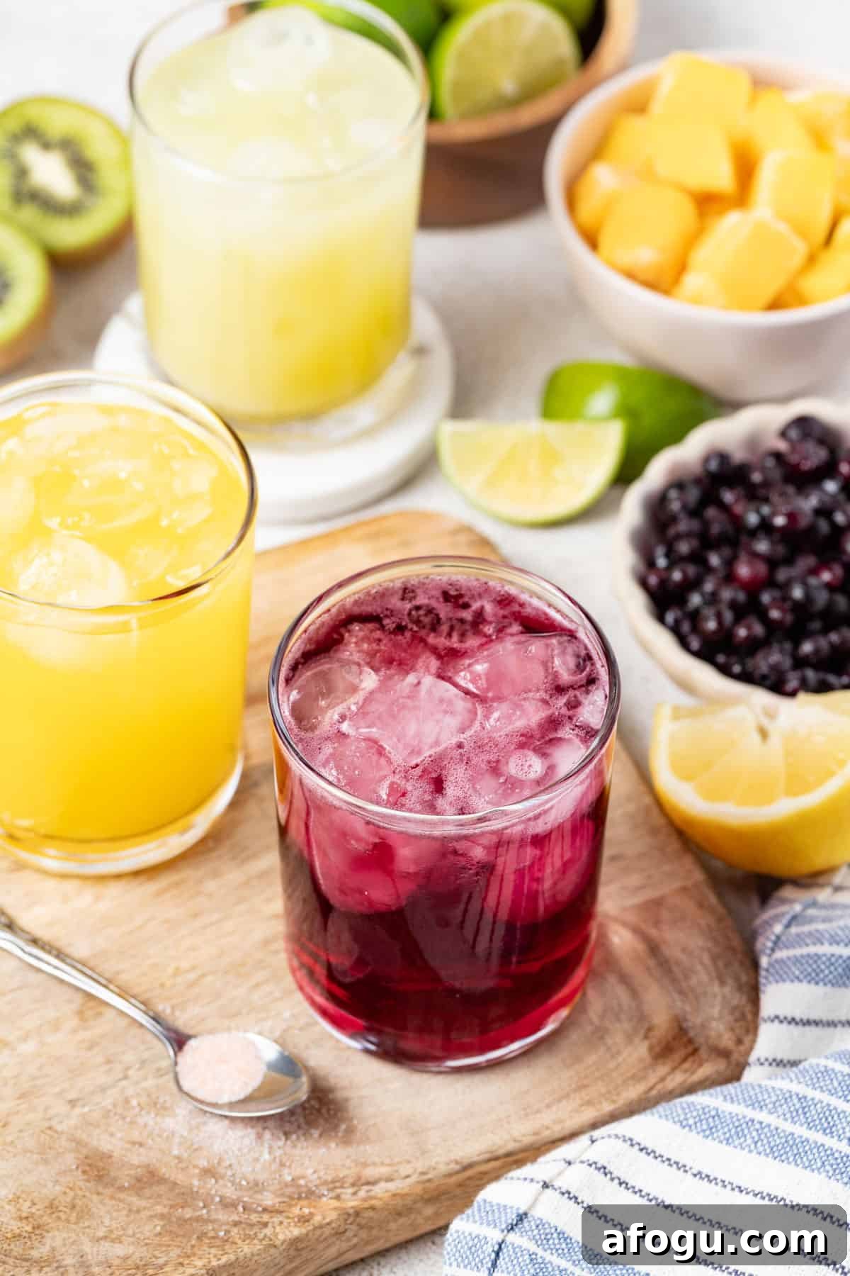 Glasses with different flavors of homemade gatorade next to berries, mango, and lemon lime.