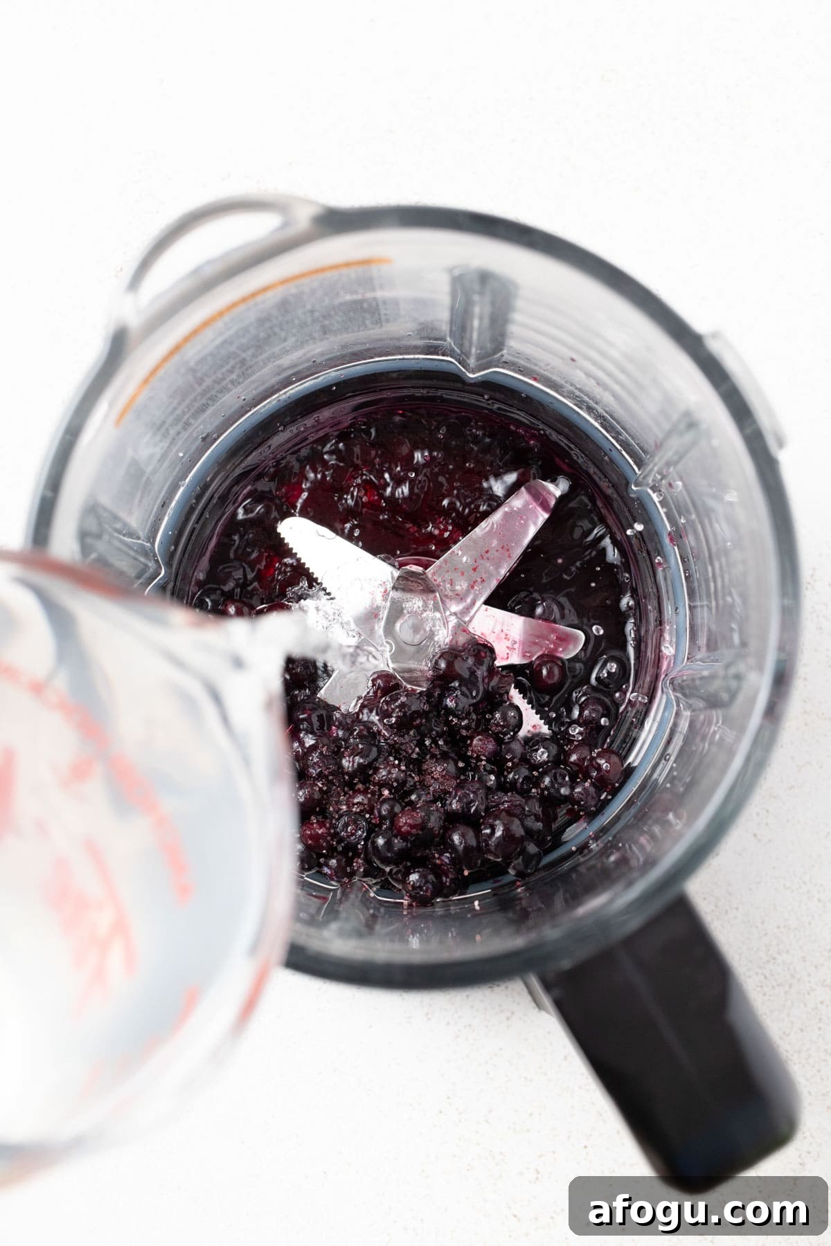 Pouring coconut water and blueberries into a blender.