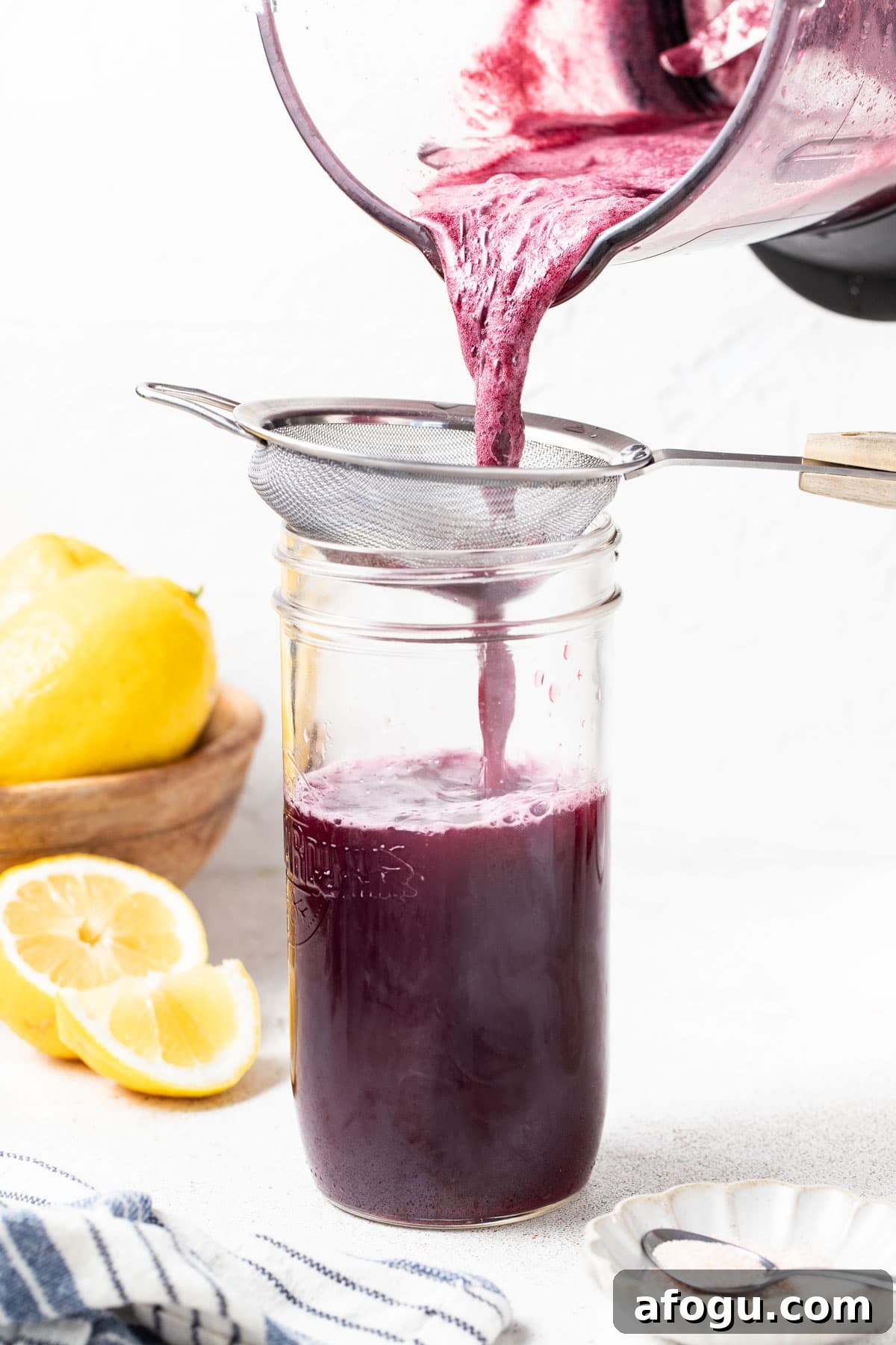 Straining blueberry coconut water mixture into a tall glass.