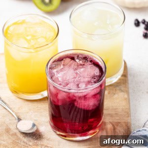 3 flavors of homemade gatorade in glasses on a wood table next to a spoon with salt.