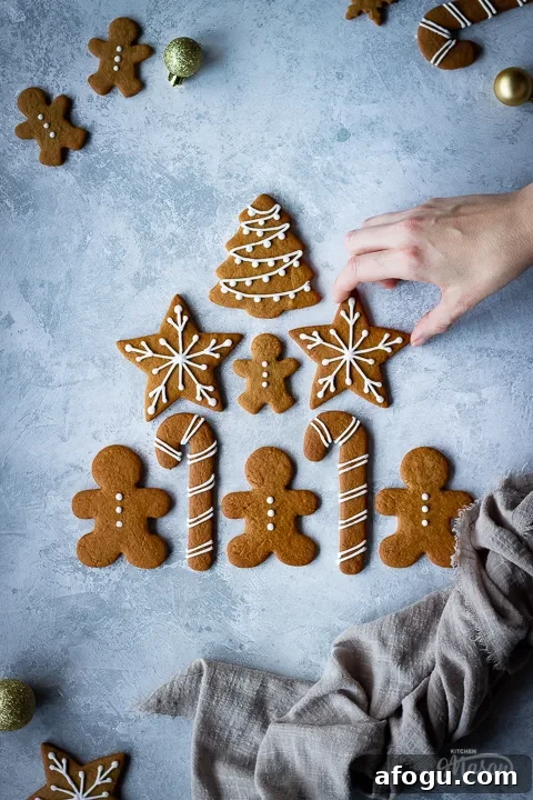 Classic Gingerbread Biscuit Recipe for Perfect Holiday Baking 8 A hand reaching in to 1 of 9 decorated gingerbread biscuits laid on a grey plaster effect backdrop in a triangle shape with a light brown linen napkin scrunched up to the side. There are more biscuits and gold baubles in the background.