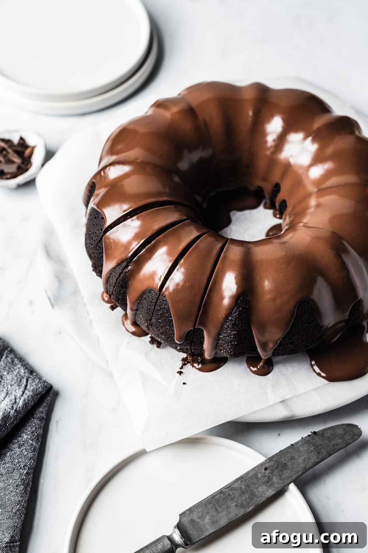 Close up of sliced chocolate olive oil bundt cake with chocolate ganache glaze on a white marble platter