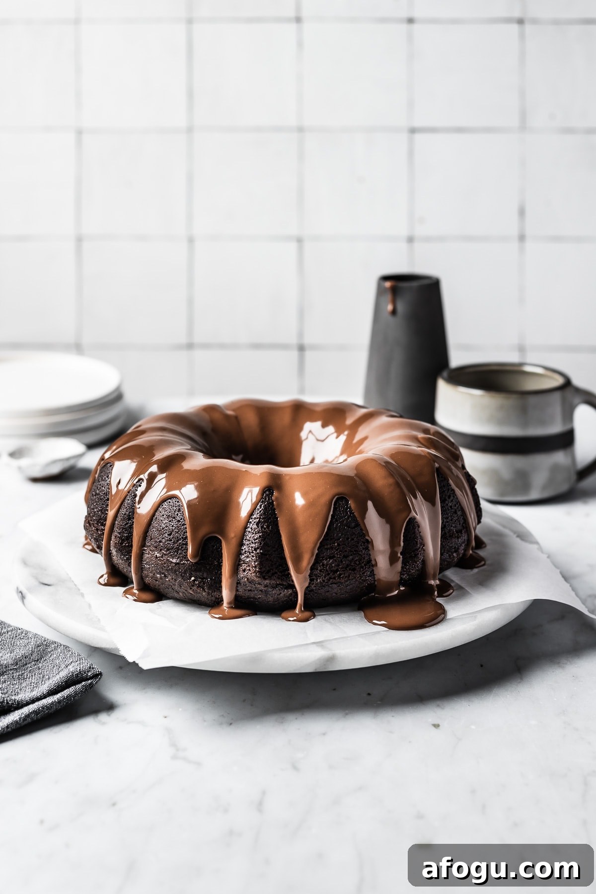 A chocolate cake drizzled with a chocolate ganache on a marble platter and marble countertop