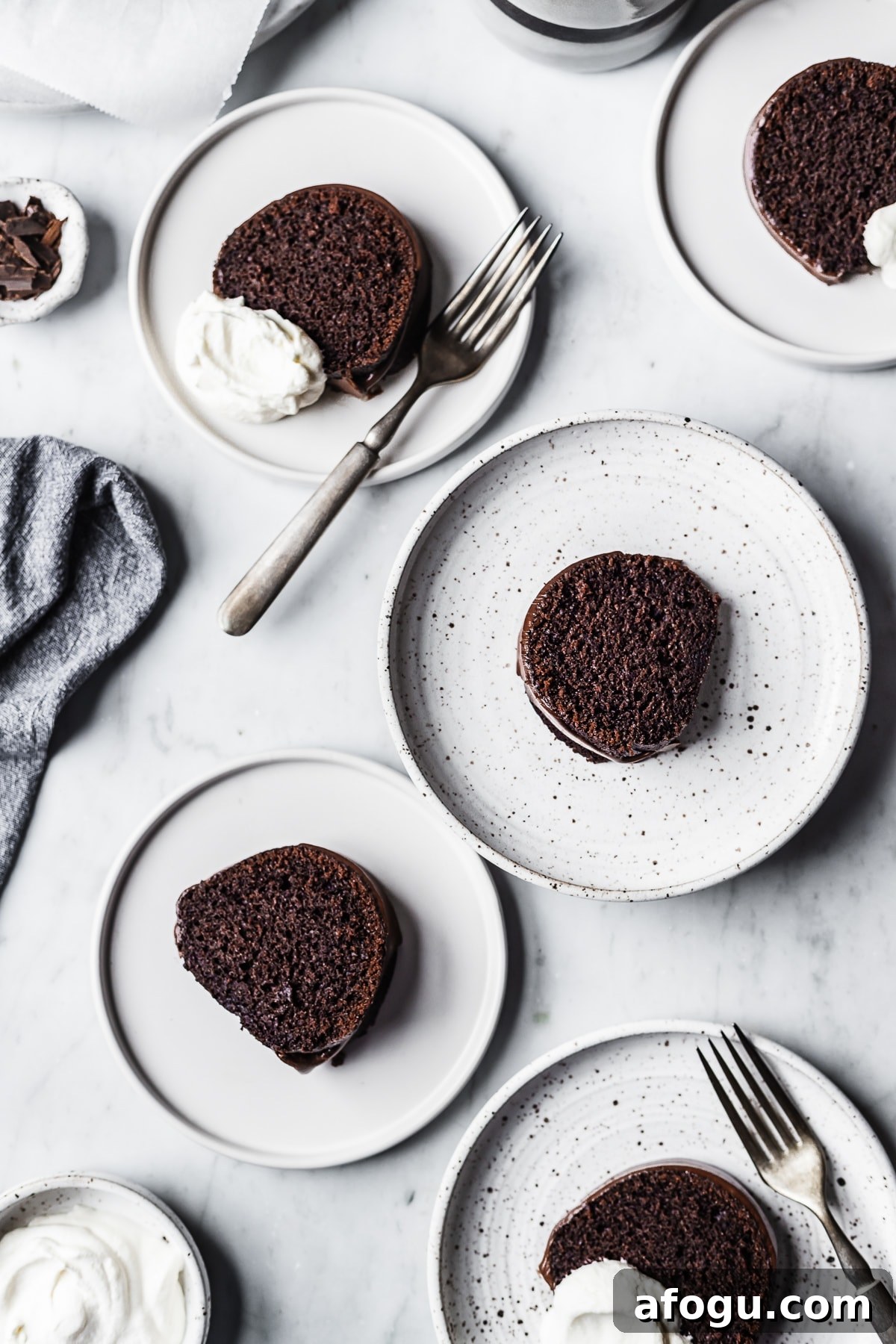 Five white plate each with a slice of chocolate bundt cake resting on a marble surface 