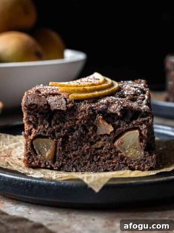 A square of chocolate pear cake from the side showing the crumb and fruit inside.