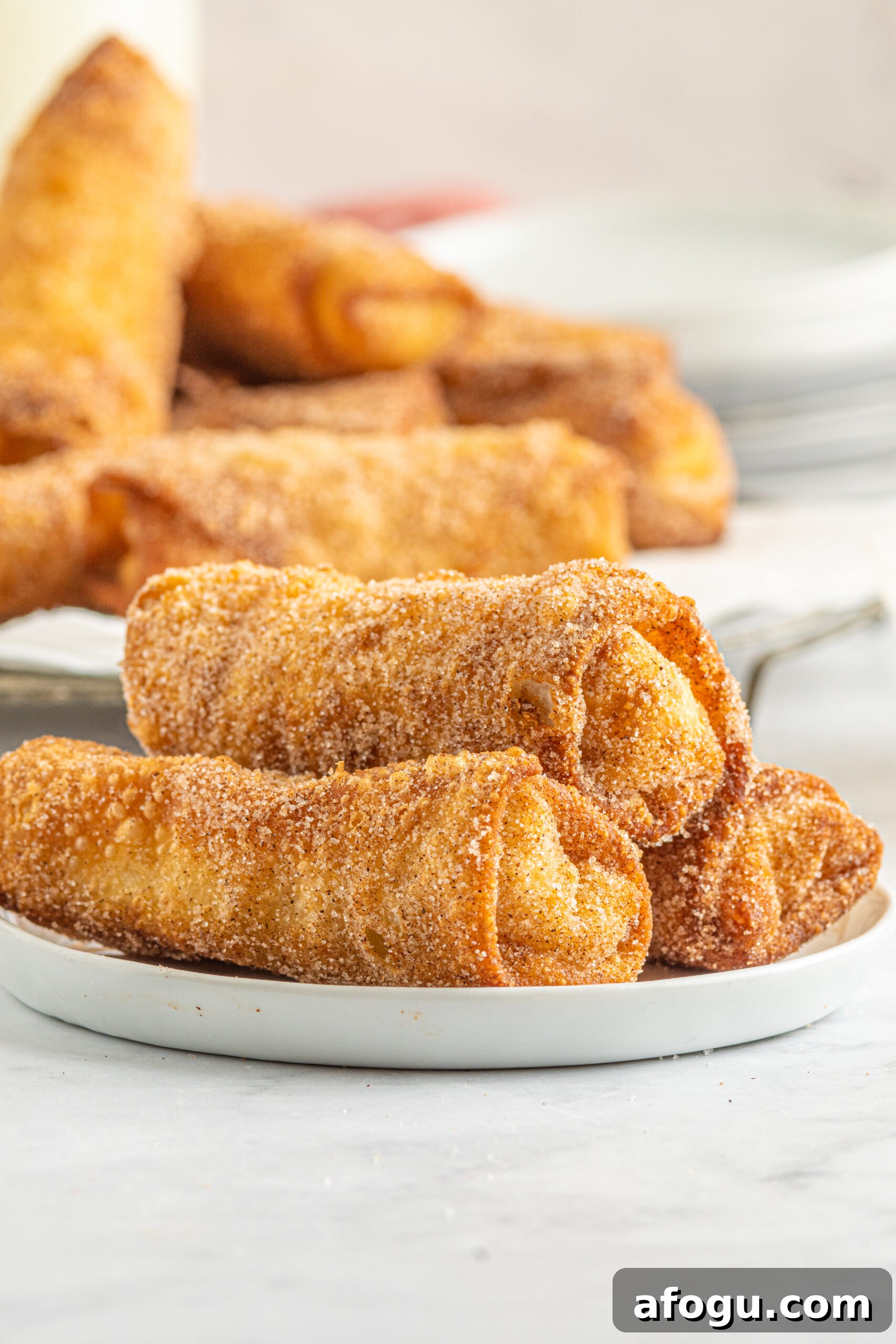 Front view of three Cheesecake Egg Rolls stacked on a white plate.