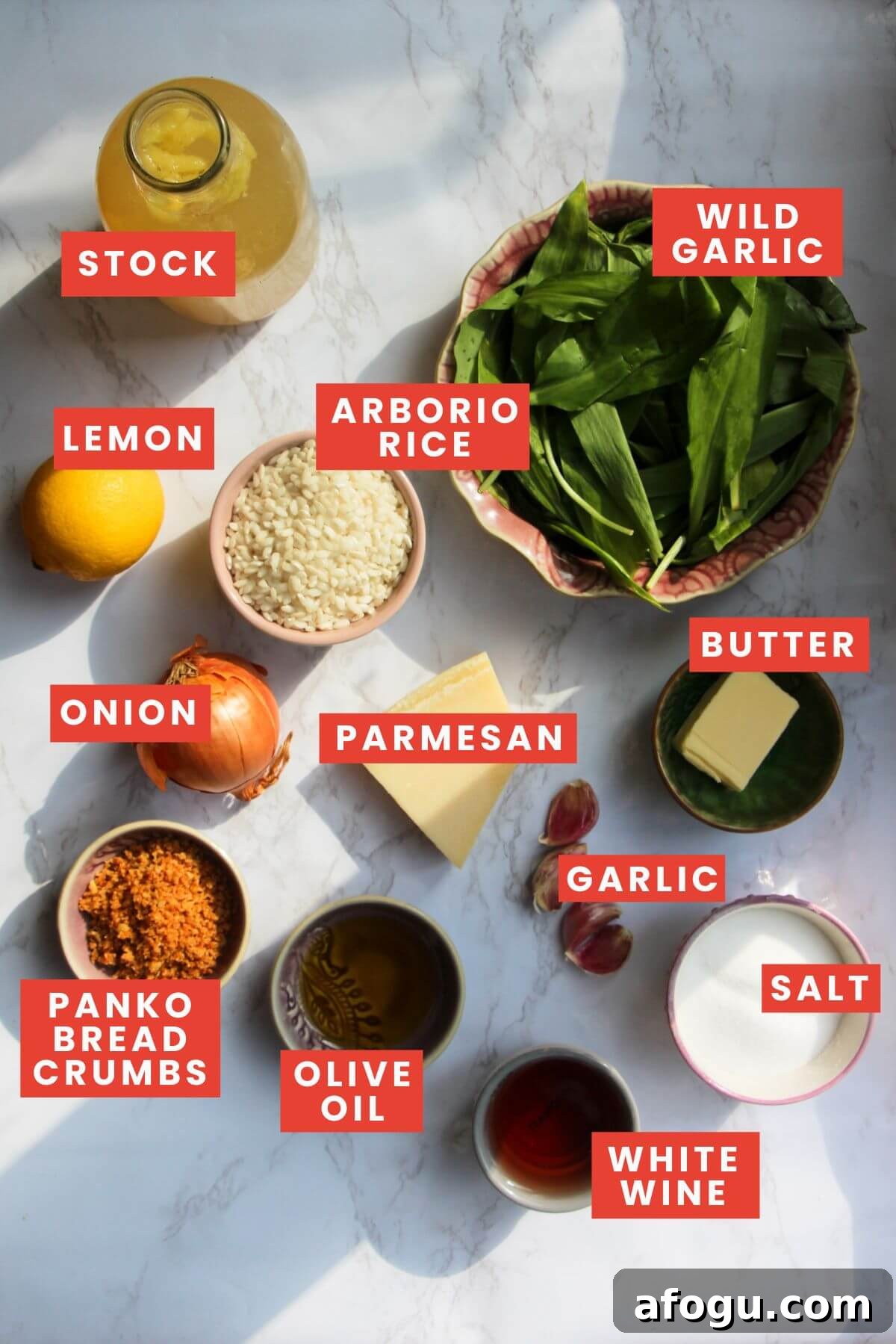 Wild garlic risotto ingredients laid out on a white marble background and labelled.
