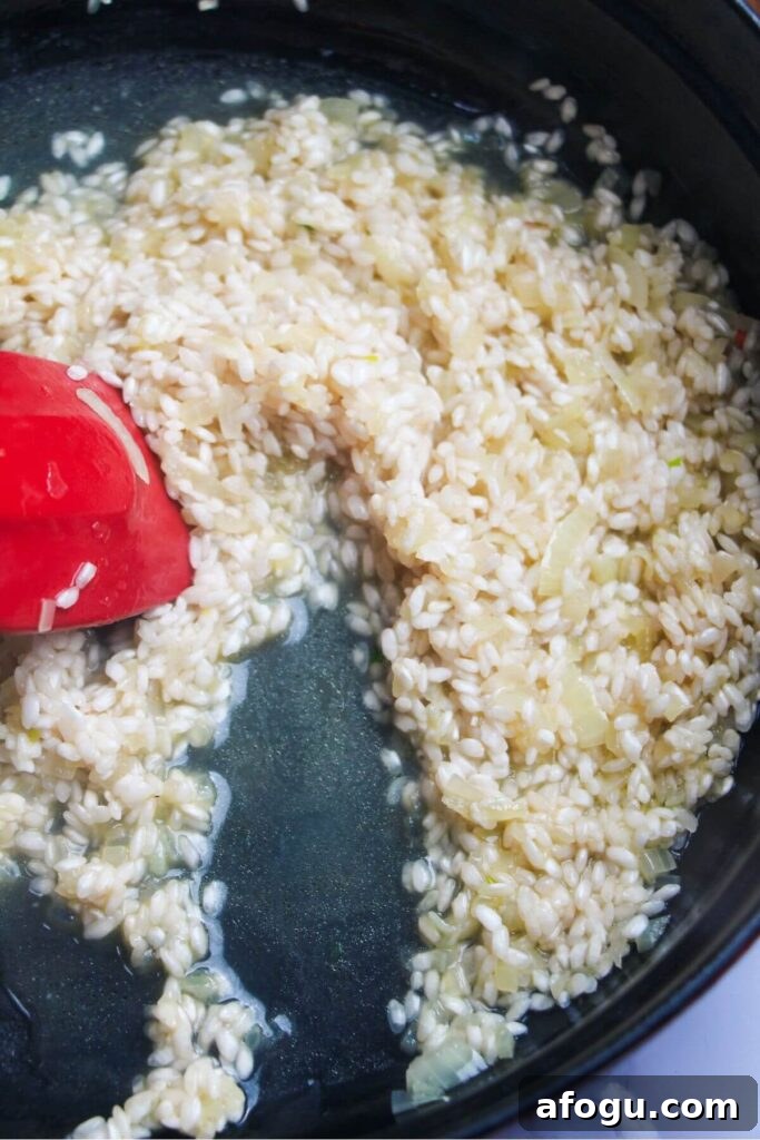Red spatula stirring risotto in a large black skillet.