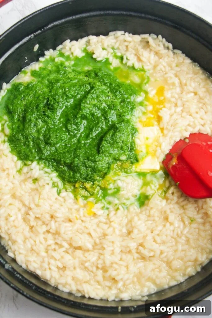Wild garlic puree and butter added to cooked risotto in a large black skillet.
