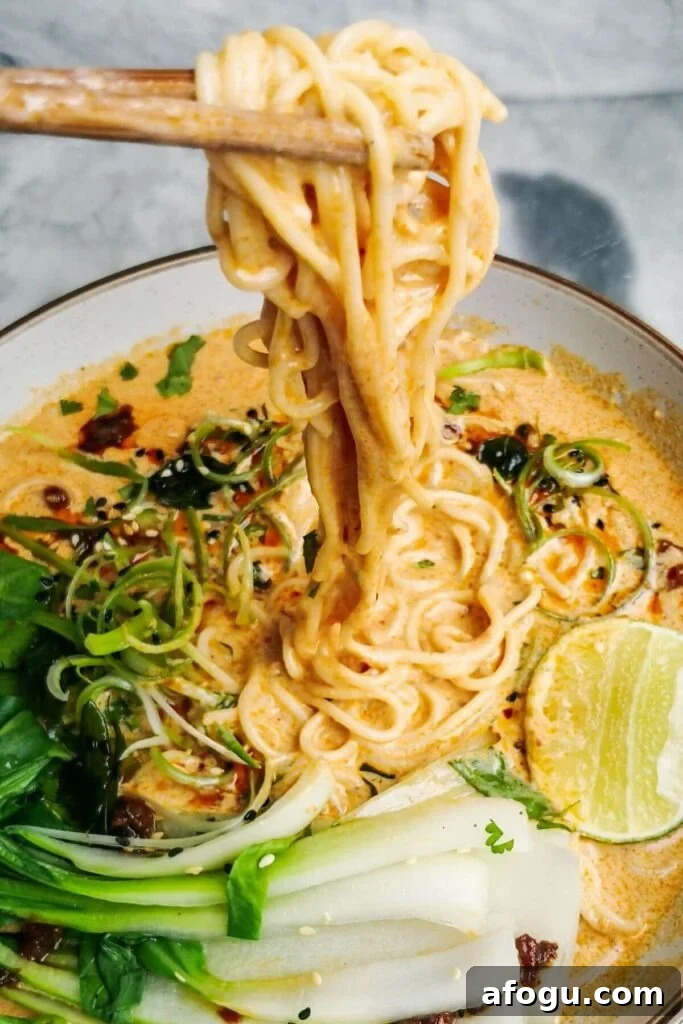 Chopsticks pulling up saucy coconut noodles in a white bowl.