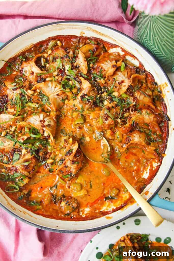 Baked dumplings in satay sauce in a skillet with chili oil on top.