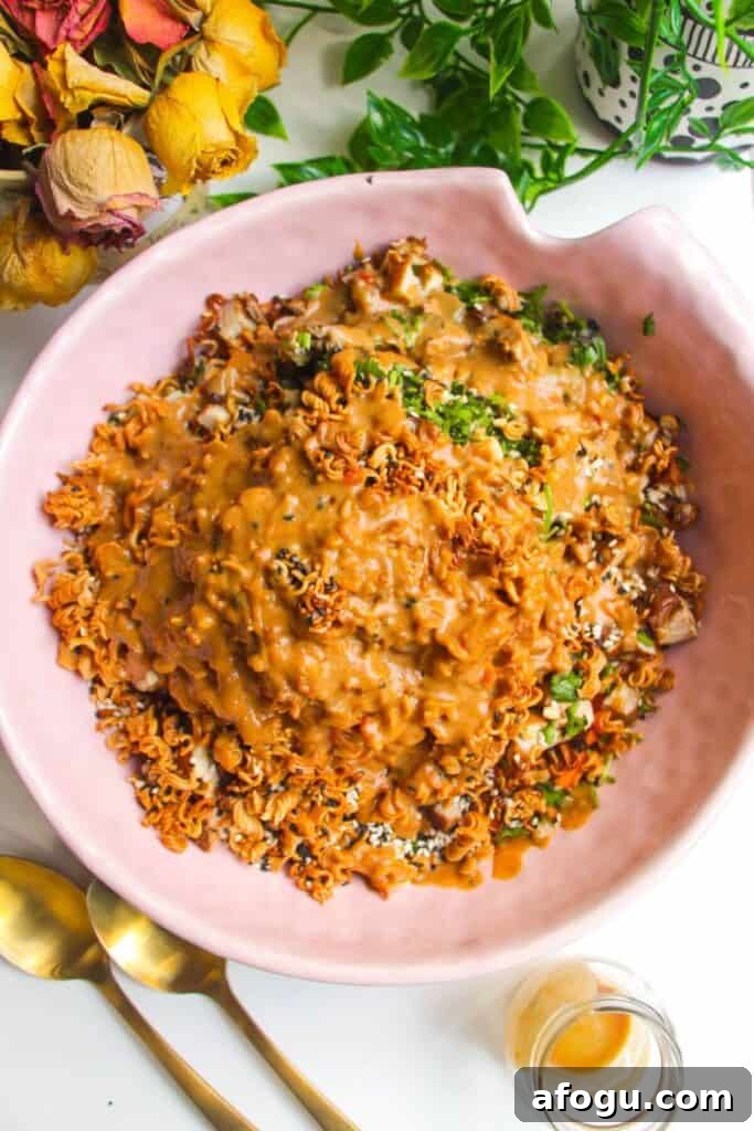 Peanut satay dressing poured over crispy ramen salad in pink bowl.