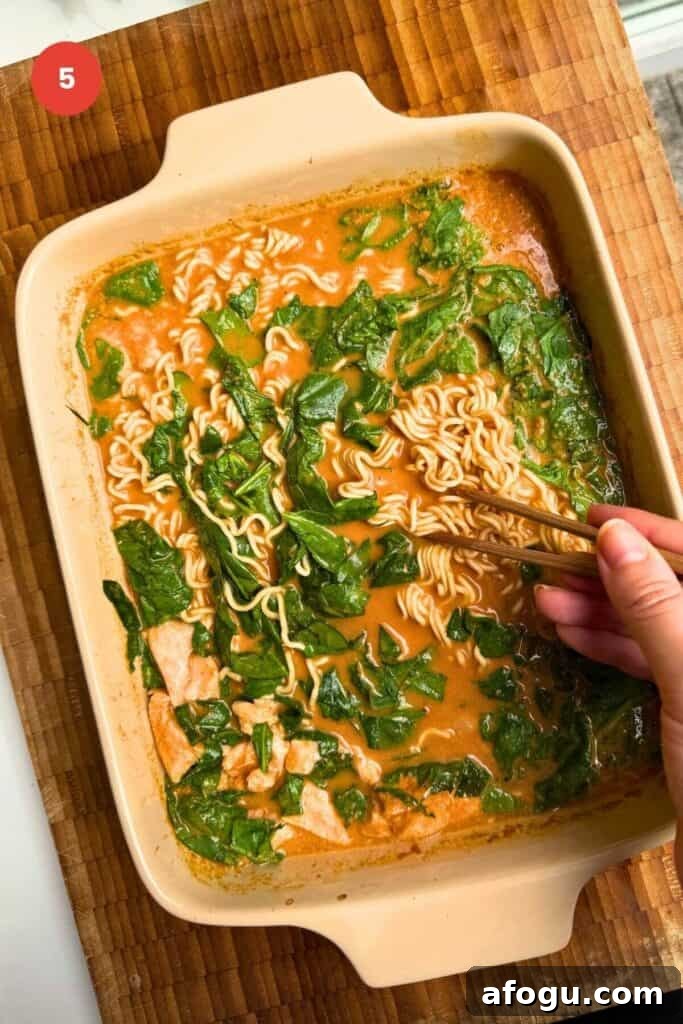 Hand holding chopsticks, mixing ramen noodles.