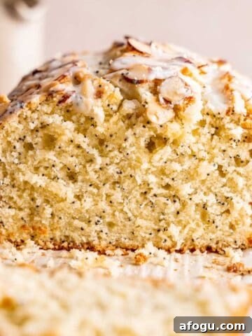 A loaf of almond poppy seed cake topped with sliced almonds and almond poppy seed glaze.
