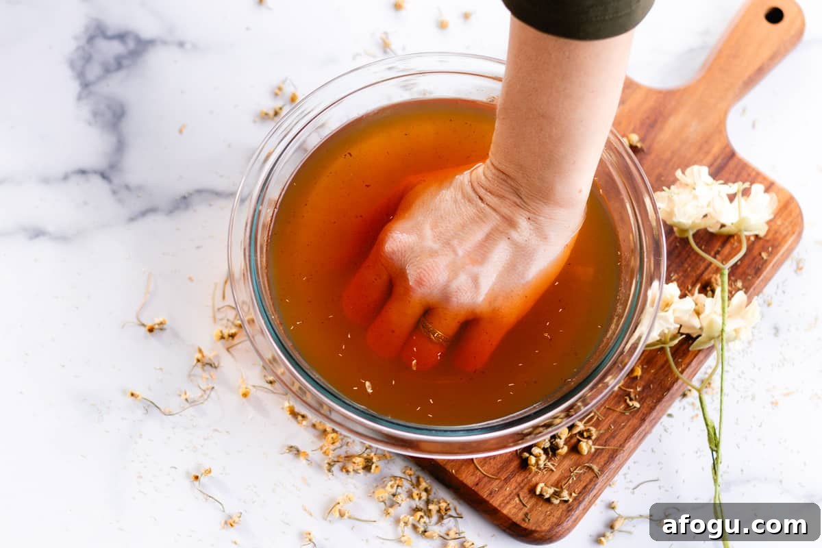 Submerging my hand into a homemade hand soak recipe on a marble table top.