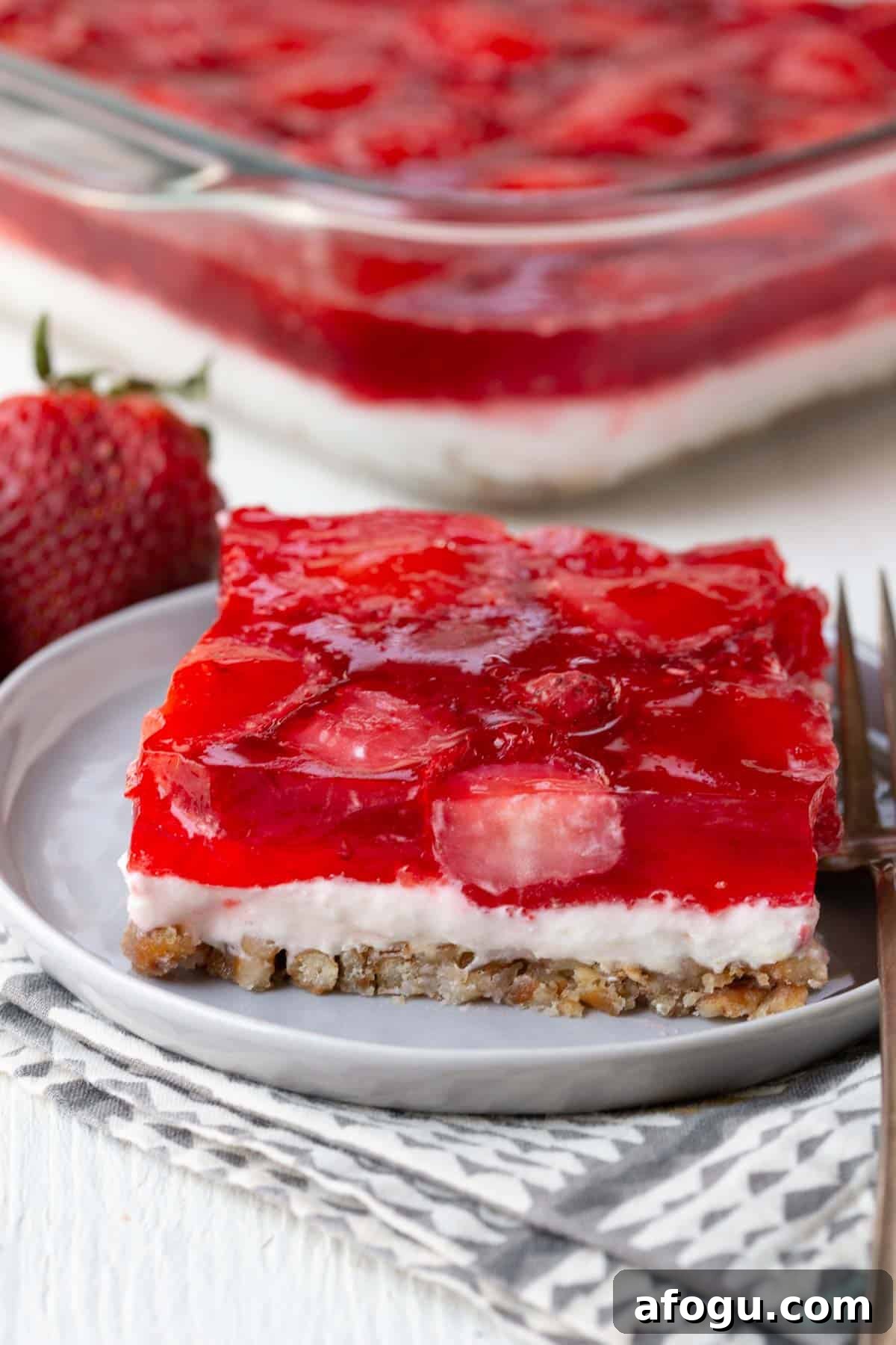 slice of layered dessert with a pretzel crust, creamy center, and strawberry jello topping.