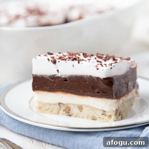 piece of chocolate delight layered dessert on a white plate on top of a blue napkin.