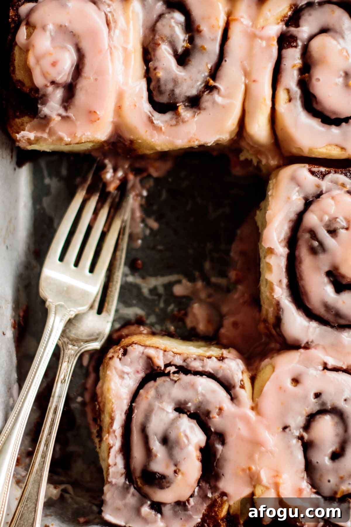 Pink Blood Orange Cinnamon Rolls with Citrus Glaze 6 Blood orange cinnamon rolls with pink glaze and two forks on a baking pan.