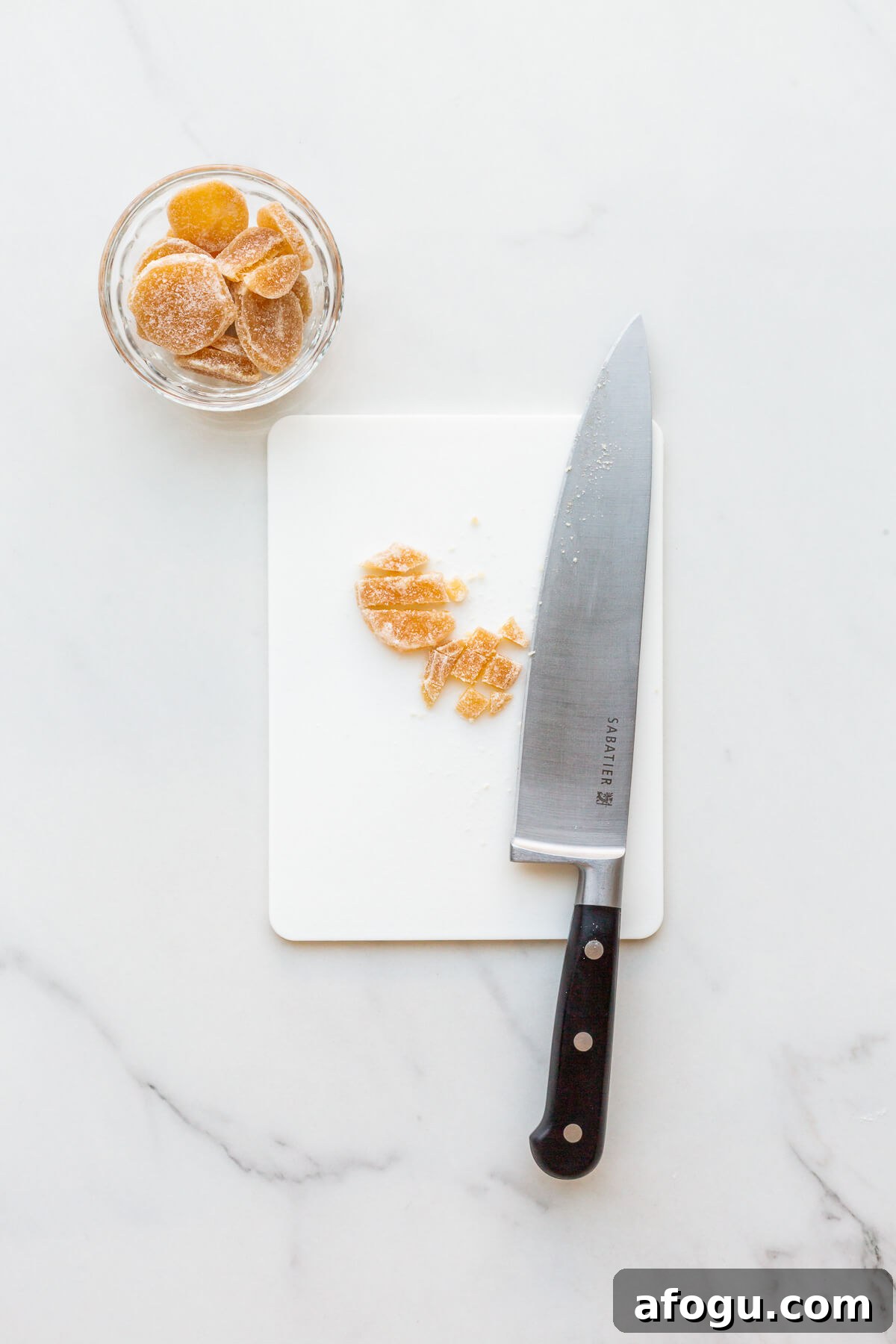 Chopping crystallized ginger with a chefs knife on a cutting board.