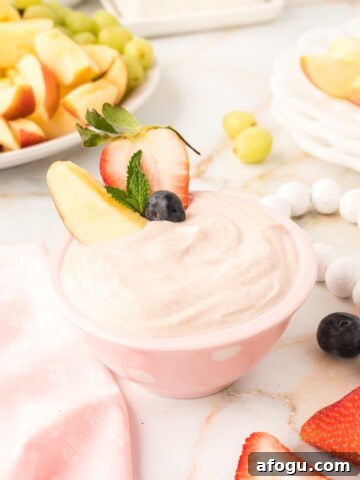 Yogurt fruit dip in a pink bowl with strawberries and apple wedge.
