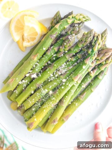 Cooked asparagus on a plate with lemon and a sprinkling of parmesan cheese