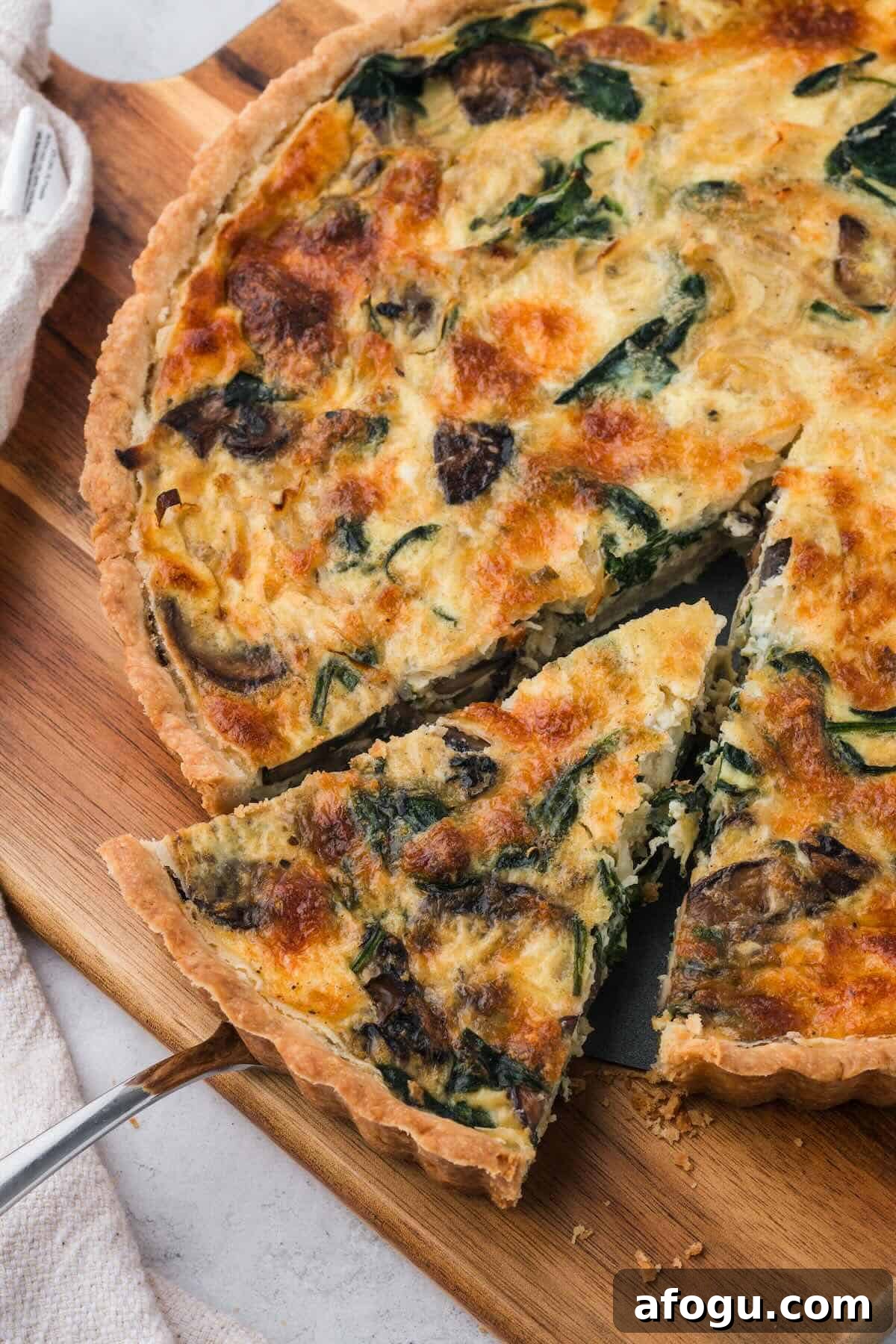 Spinach Mushroom Quiche Recipe — Flaky Crust, Creamy Filling 10 A sliced spinach and mushroom quiche on a cutting board.