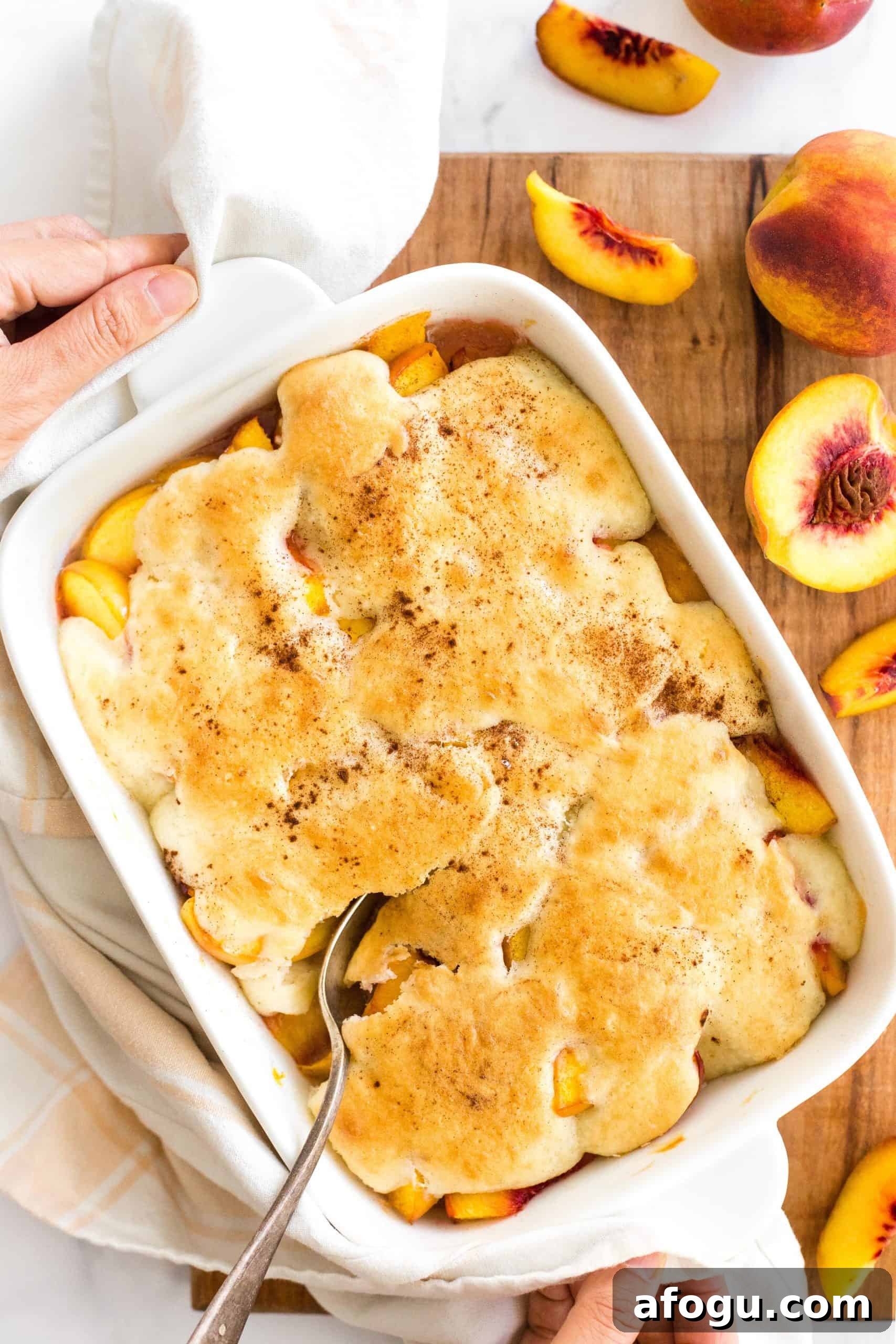 Easy Gluten-Free Dairy-Free Peach Cobbler Recipe (Vegan) Two hands reaching for a cobbler-filled baking dish.