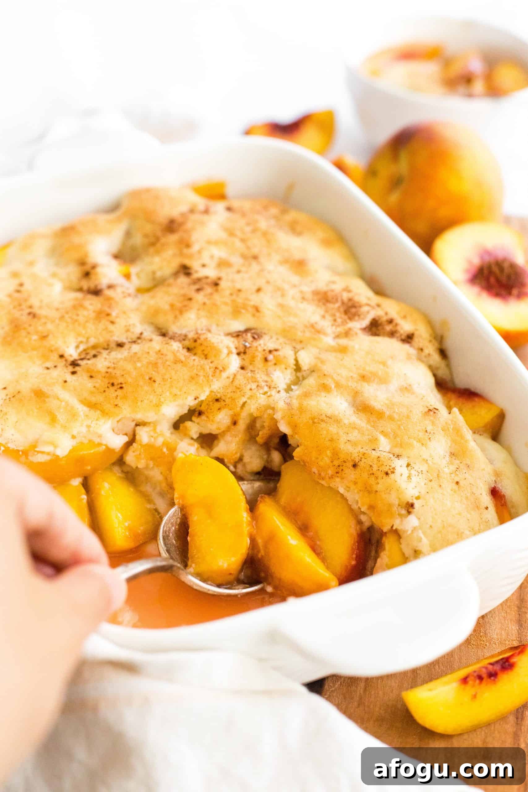 Easy Gluten-Free Peach Cobbler (Dairy-Free, Vegan) Spooning gluten-free peach cobbler from a baking dish.