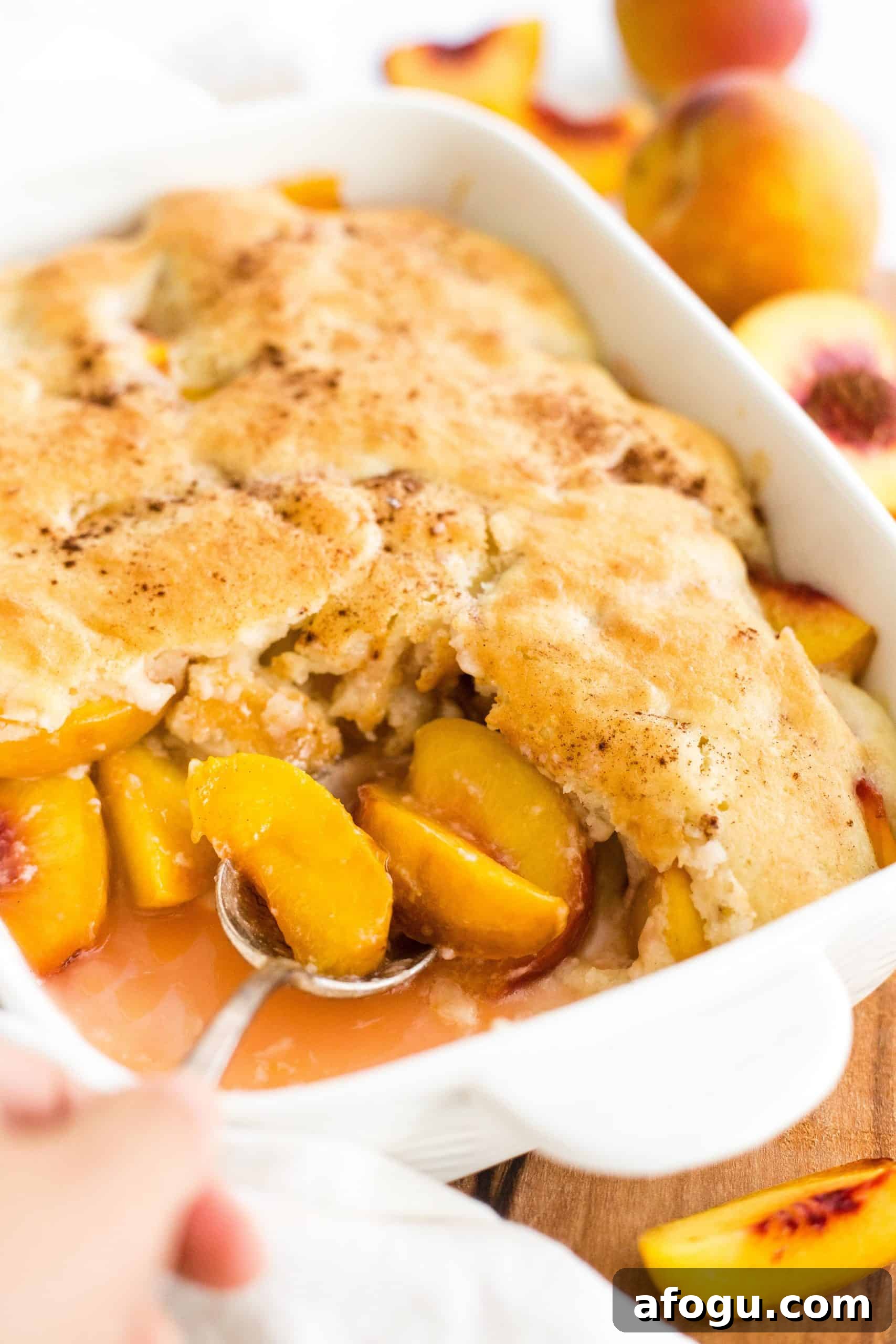 Gluten and Dairy Free Peach Cobbler Hand reaching for a spoon in a dish of half-eaten gluten-free peach cobbler.