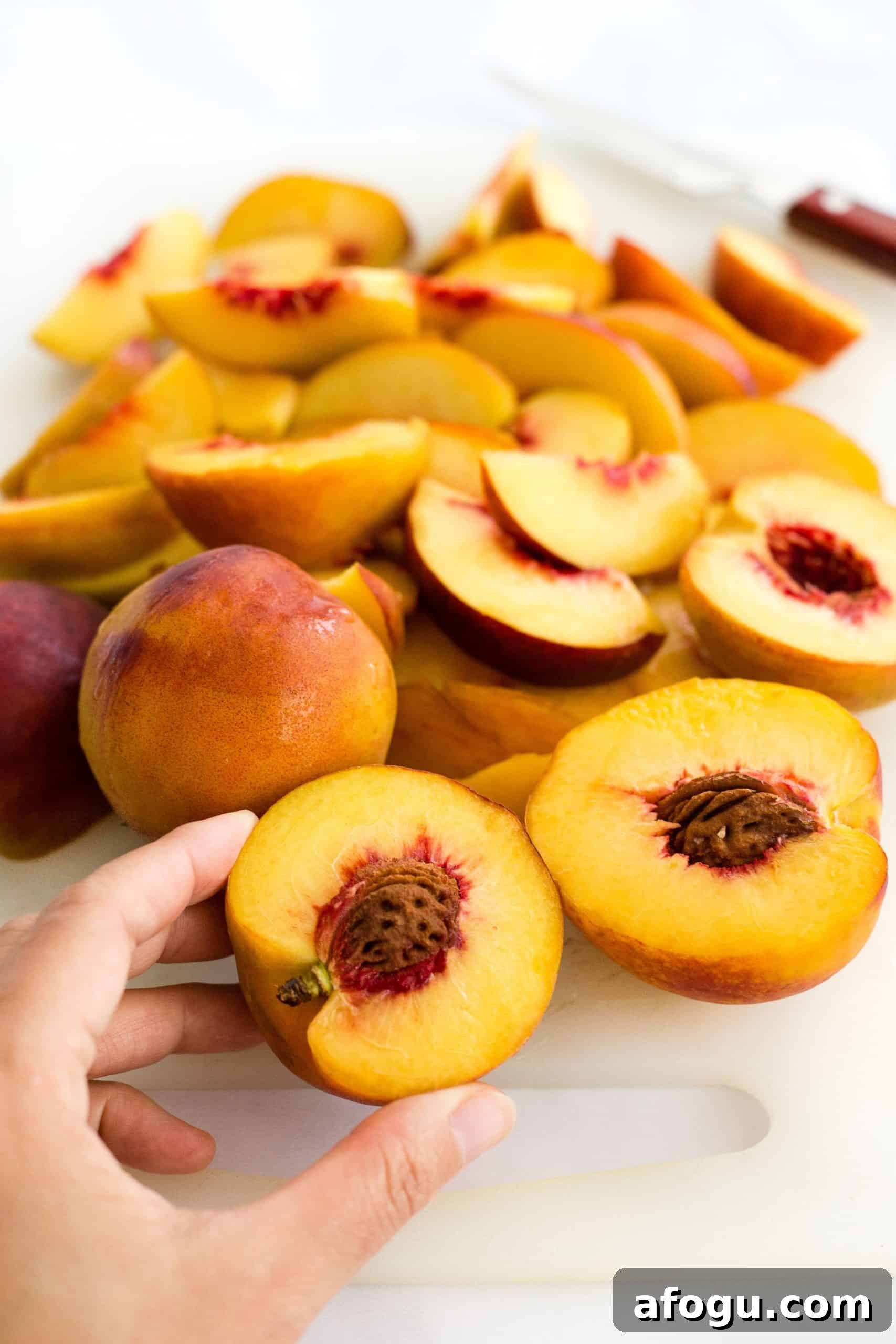 Gluten-Free Dairy-Free Cobbler Hand holding a half-cut peach with other peaches in the background.