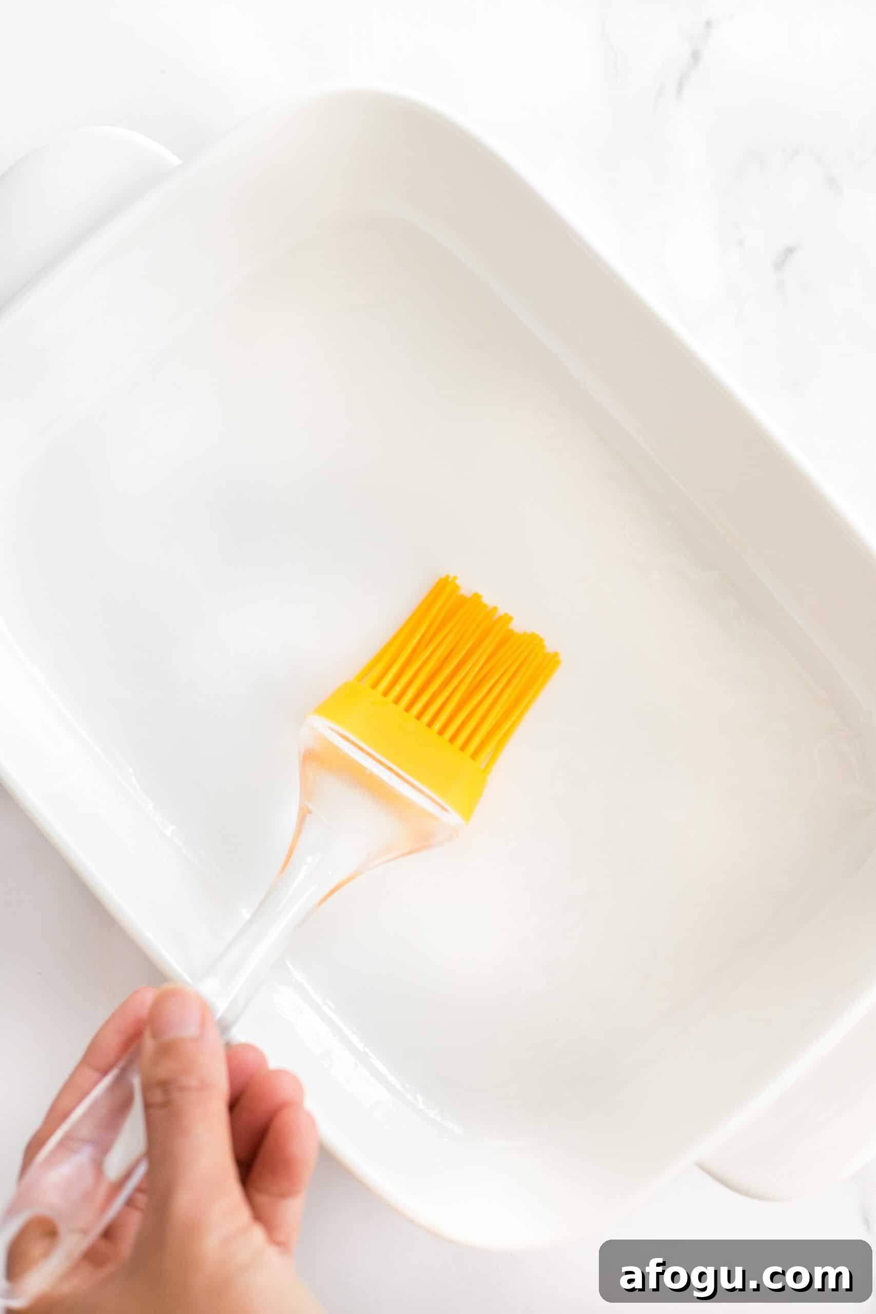 Dairy-Free Peach Cobbler (Dairy-Free, Vegan) Brushing a white baking dish with oil.