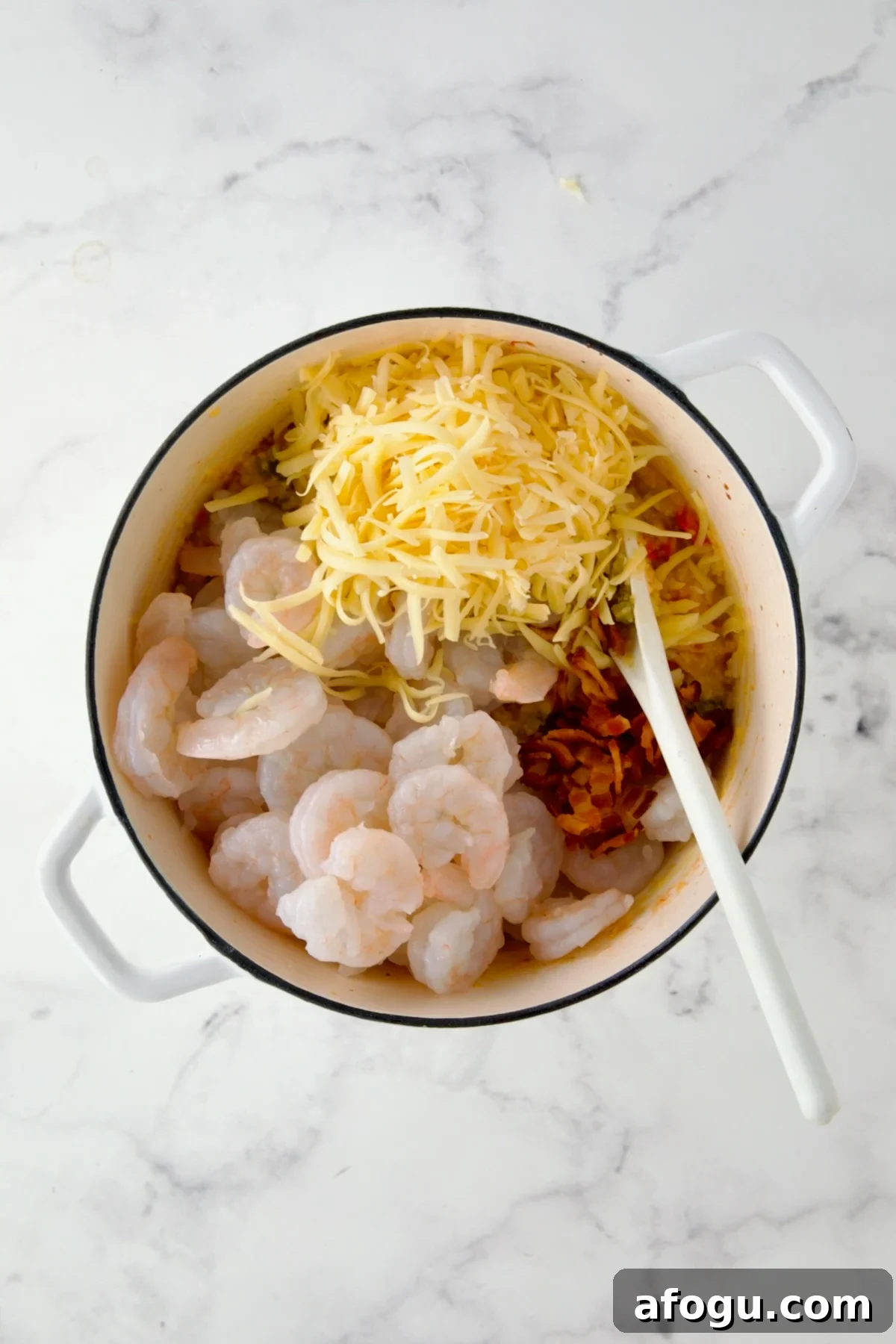 Shrimp and cheese added to vegetable and grits combination in white Dutch oven.