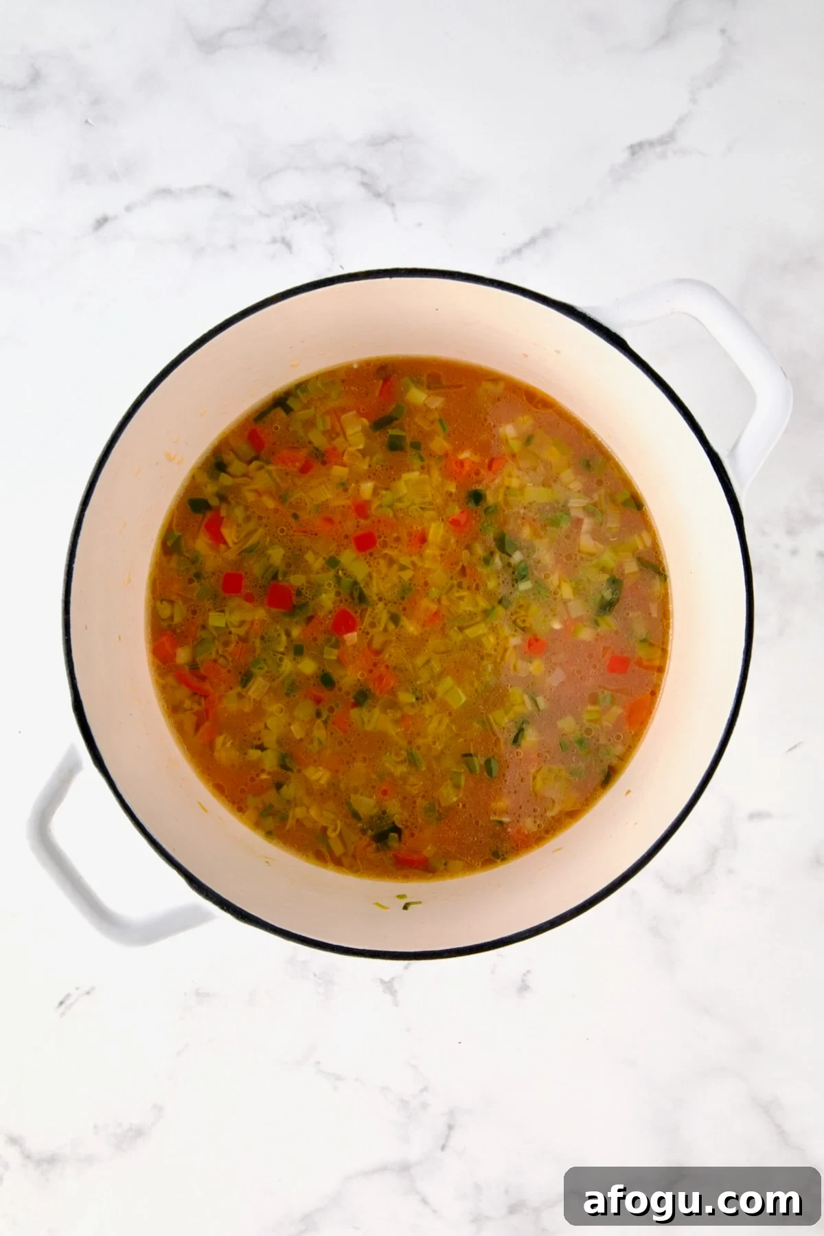 Broth added to vegetables in white Dutch oven.