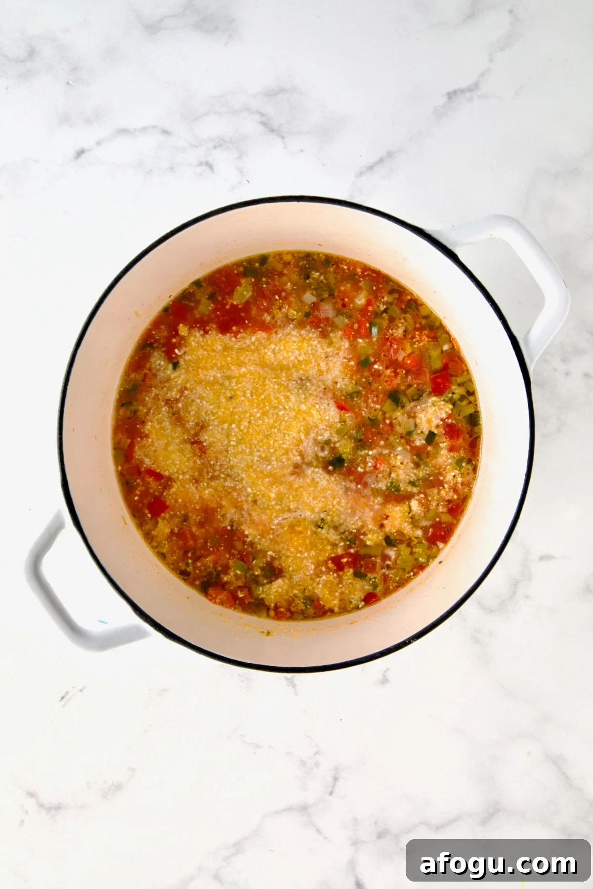 Grits added to vegetables and broth in white Dutch oven before being stirred in.