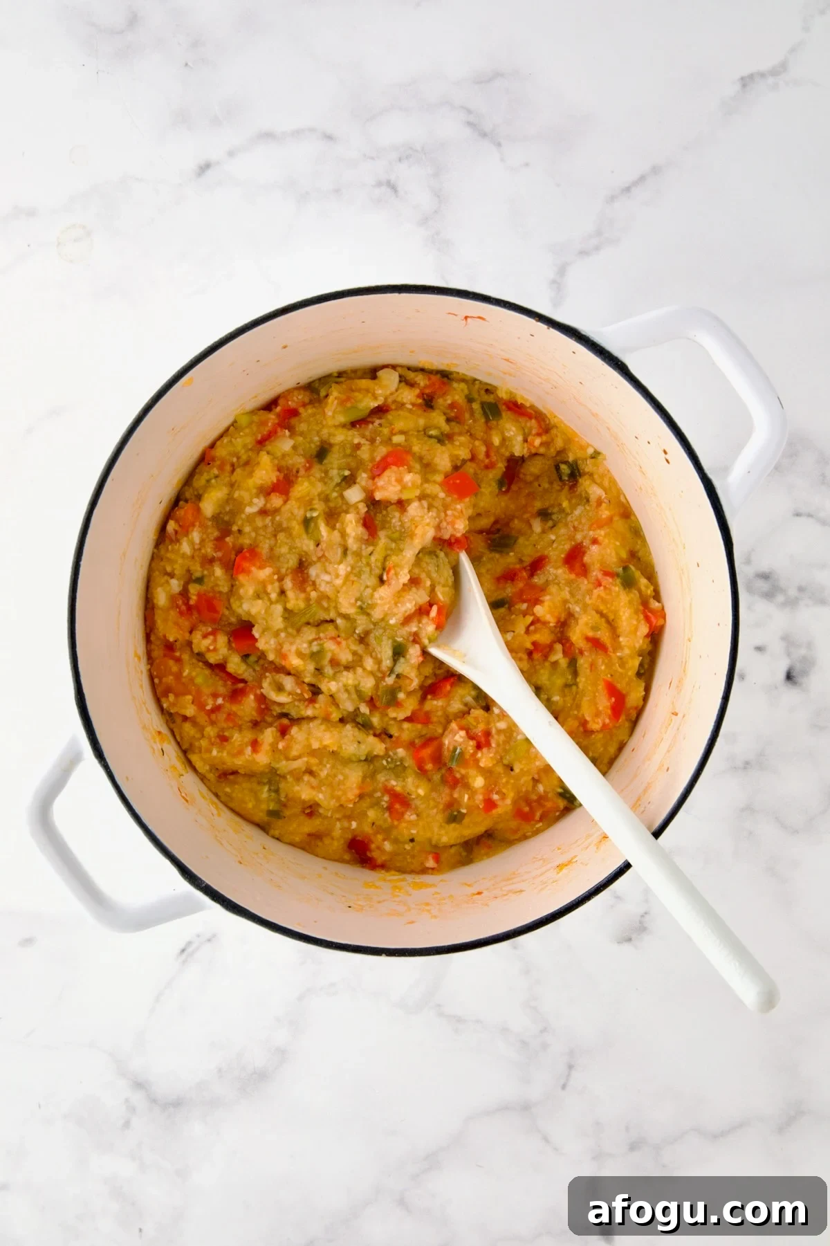 Cooked grits and vegetables in white Dutch oven.