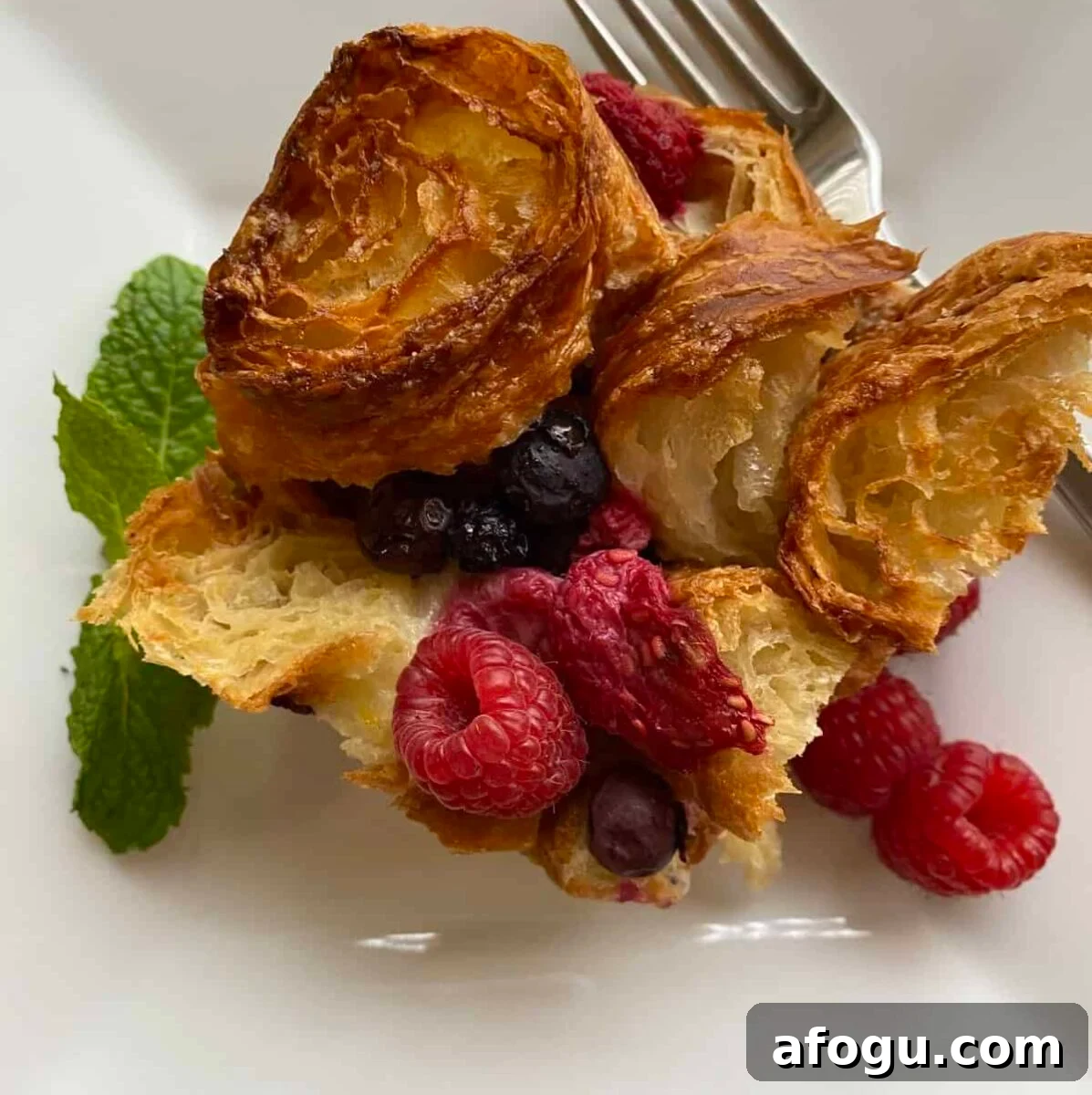 A serving on a plate with a sprig of mint and fresh raspberries.