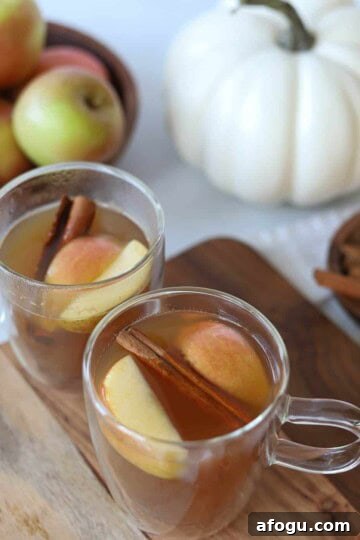 Two hot apple cider bourbons topped with fresh apple and cinnamon sticks.